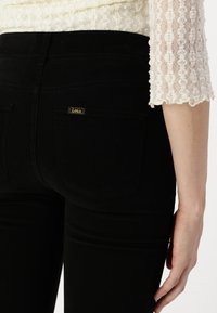Jeans negri din denim cu o textură netedă, talie înaltă și etichetă galbenă contrastantă "Lois" pe buzunarul din spate, având un design ajustat.