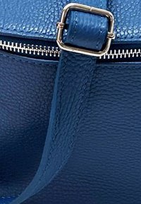 Donkerblauwe leren handtas met een gestructureerde afwerking. Beschikt over een vierkante gesp in goudkleur en een metallic ritsaccent. Het hengsel is glad.