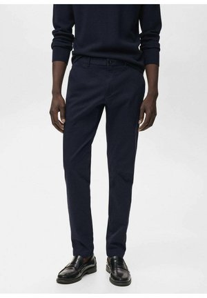 Pantalones ajustados azul marino en una tela suave, con un corte slim, bolsillos delanteros y cierre de botón, combinados con mocasines negros.