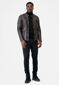 Braune Lederjacke mit Reißverschlusstaschen, schwarzem Rollkragenpullover, schwarzen Jeans und schwarzen Schnürstiefeln. Glatte Textur und taillierte Passform.