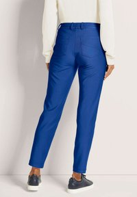 Blauwe stretchy broek met een taps toelopende pasvorm, elastische tailleband en twee achterzakken. Gecombineerd met casual sneakers voor een ontspannen look.