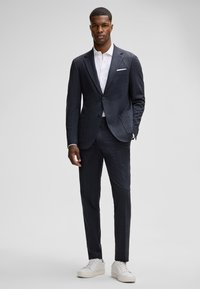 Donkere geruite pak met slim fit, voorzien van een gelapelde kraag en twee knopen, gecombineerd met een wit shirt en witte sneakers. Glad, textielachtig materiaal.