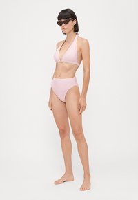 Bikini cu dungi roz și alb, cu guler halter, având un detaliu central în formă de inel și slip cu talie înaltă. Material neted, fără modele vizibile.