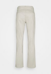 Pantalon beige à jambes droites avec poches passepoilées à l'arrière, passants pour ceinture et une ceinture propre, vu de dos sur un fond uni.