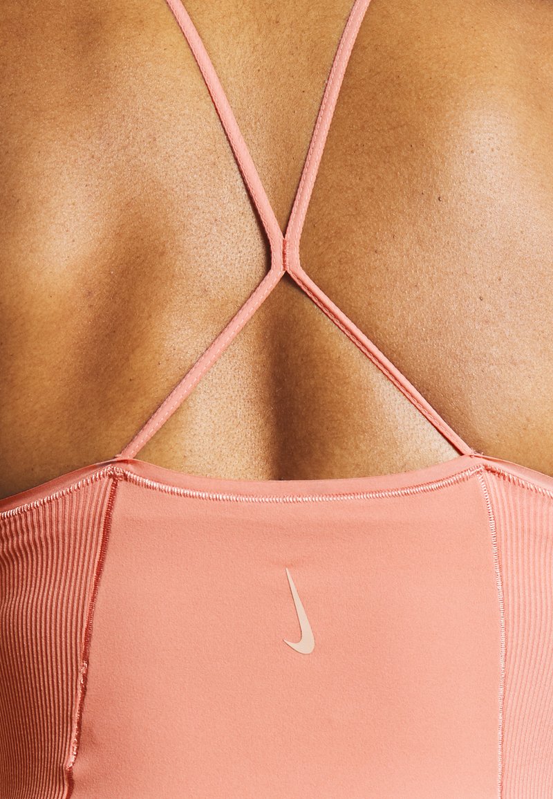 Top deportivo de Nike en coral claro, con un diseño de tirantes cruzados en la parte posterior y un pequeño logo en la parte inferior izquierda. Tela suave y elástica.