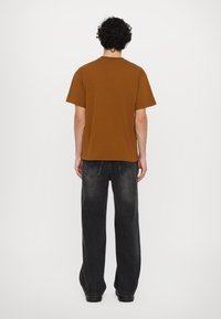 Brown short-sleeve t-shirt, back view, paired with black wide-leg jeans. Smooth texture, casual fit, and simple design.