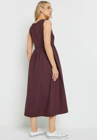Vestido maxi sin mangas color burdeos con un corpiño ajustado y falda fruncida. Tejido ligero, detalles de bolsillos laterales, combinado con zapatillas blancas.