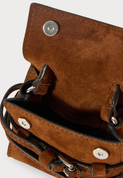 Borsa a tracolla in suede marrone aperta, con bottoni a pressione magnetici, dettagli della tracolla in pelle nera e scomparto interno vuoto.
