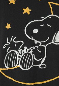 Black fabric t-shirt featuring a white and yellow graphic of Snoopy and Woodstock with stars, highlighting playful cartoon design and textures.