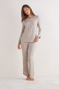 Zacht beige loungewear-set bestaande uit een langemouwen top en bijpassende broek. Textuurpatroon overal, met een relaxte pasvorm en een gladde afwerking.