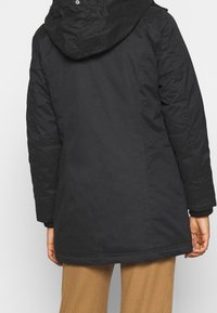 Black insulated parka with a hood, featuring a smooth texture and a knee-length design. Cuffs have a ribbed detailing.