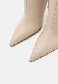 Escarpins en cuir beige à bout pointu avec une texture lisse et des détails de couture subtils, dotés d'un talon aiguille mince.