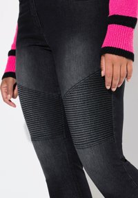 Leggings de mezclilla negra con paneles acanalados a lo largo de los muslos, con una textura suave y un diseño ajustado. La cinturilla es sin adornos.
