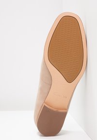 Chaussure en cuir beige à texture lisse, dotée d'une semelle marron clair, d'un bout rond et de détails de couture subtils sur le côté.