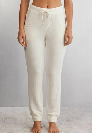 Crème-kleurige geribbelde loungebroek met een elastische tailleband en verstelbare trekkoord. Bevat zijzakken en aansluitende boorden bij de enkels.