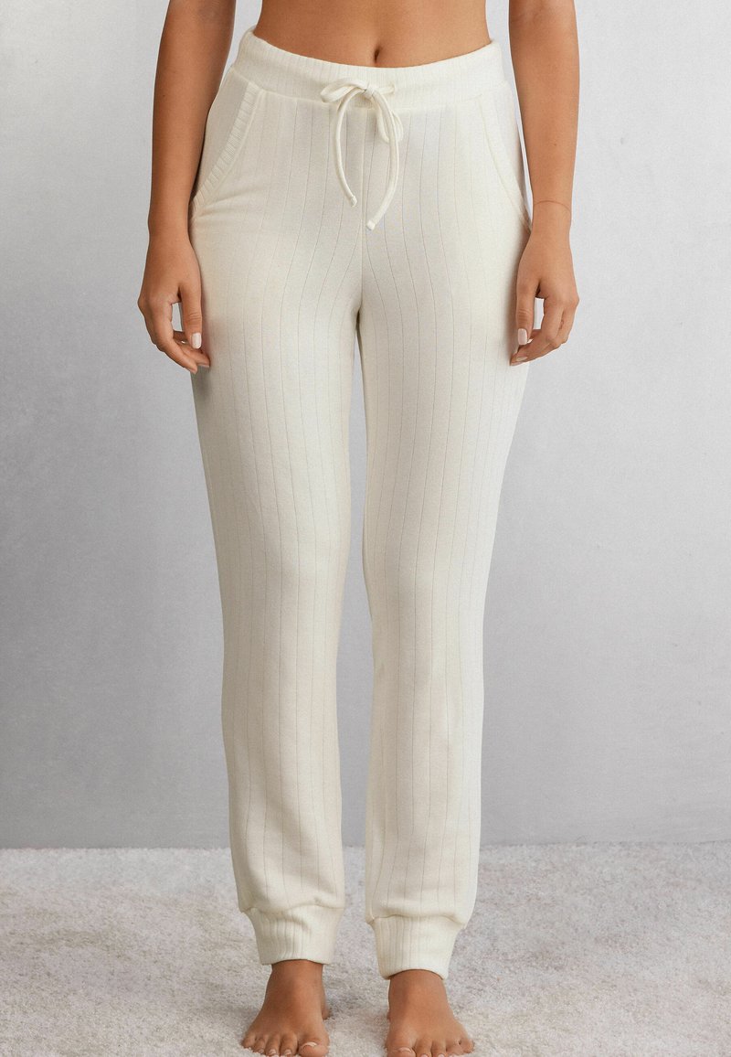 Crème-kleurige geribbelde loungebroek met een elastische tailleband en verstelbare trekkoord. Bevat zijzakken en aansluitende boorden bij de enkels.
