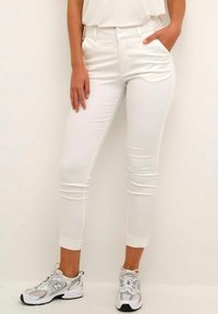 Witte slim-fit broeken met voorzakken, middelhoge taille en een gladde textuur, gecombineerd met grijze en witte sportschoenen.