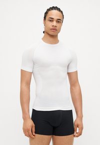 Short-sleeve, form-fitting white athletic shirt with a smooth texture and subtle pattern on the front, paired with black shorts.
