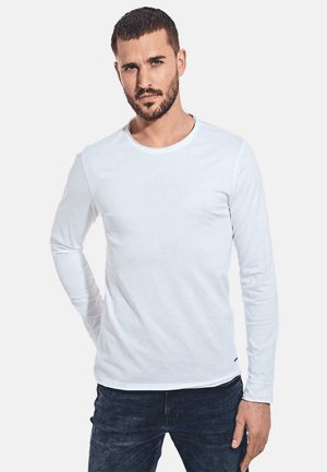 White long-sleeve shirt with a round neckline, slim fit, and smooth texture, paired with dark denim jeans. No patterns or accents visible.