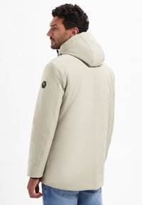 Lichtbeige waterdichte jas met een kap, voorzien van een ritssluiting aan de voorkant, zijzakken en een cirkelvormig logo op de linker mouw.