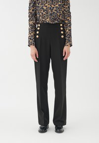 Schwarze maßgeschneiderte Hose mit hoher Taille, ausgestattet mit großen goldenen Knöpfen auf der Vorderseite und einem glatten, strukturierten Stoff.