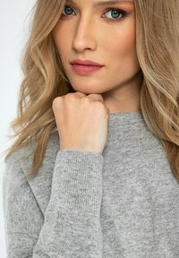 Grijze gebreide trui met geribbelde boorden, voorzien van een klein logo op de mouw. Gladde textuur, klassieke ronde hals en een casual pasvorm.