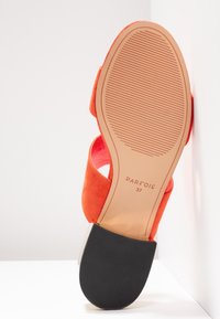 Sandale en daim orange avec une semelle texturée, un talon bloc noir, et la taille 37 marquée sur la semelle, visible vers le haut.