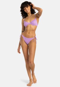 Set di bikini viola composto da un top bralette leggermente imbottito con spalline regolabili e un paio di slip a vita bassa con lacci laterali coordinati. Texture liscia.