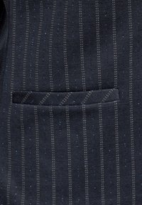 Tessuto blu scuro con righe verticali in tonalità più chiare e una leggera lucentezza, dotato di una tasca sul lato sinistro.