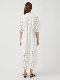 Λευκό δαντελένιο φόρεμα με floral κοψίματα, κοντομάνικα μανίκια, σφιχτή μέση και μήκος μέχρι το μισό μοσχάρι. Φορεμένο με μαύρες επίπεδες σανδάλια.