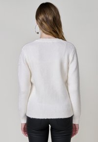 Weißer Strickpullover mit strukturiertem Finish, ausgestattet mit gerippten Bündchen und Saum. Das Design hat eine lockere Passform und wird mit schwarzen, eng anliegenden Hosen kombiniert.