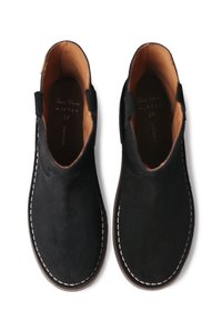 Un par de botas de tobillo de ante negro con forro interior beige, costuras blancas a lo largo de los bordes de la suela y lengüetas de agarre en los laterales, talla 37.