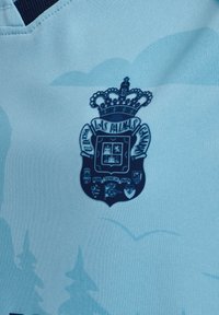 Ljusblått tyg med mörkblå Las Palmas fotbollsklubbens märke som har en krönt sköld och små emblemdetaljer.