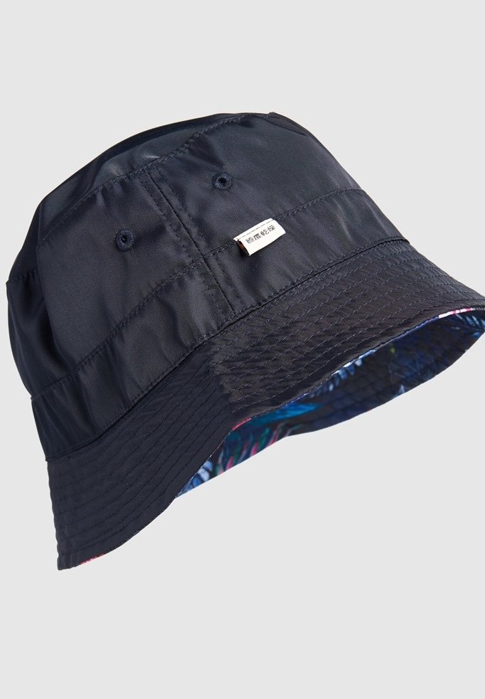 Chapeau bob bleu marine avec des trous de ventilation cousus et une petite étiquette blanche, montrant une doublure intérieure colorée à motifs sous le bord.