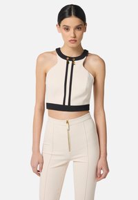 Top tagliato, senza maniche, in crema con dettagli neri e accessori dorati. Presenta un collo alto e due strisce verticali nere.