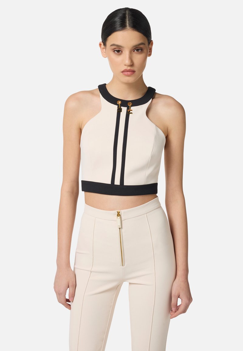 Top tagliato, senza maniche, in crema con dettagli neri e accessori dorati. Presenta un collo alto e due strisce verticali nere.