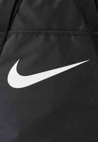 Fekete szövet táska, amelyen jól látható fehér Nike swoosh logó található, sima textúrával és erős varrással a szélén.
