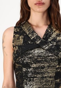 Rochie neagră cu un model texturat aurie, design fără mâneci și decolteu încrucișat, confecționată dintr-un material neted cu un strălucire subtilă.