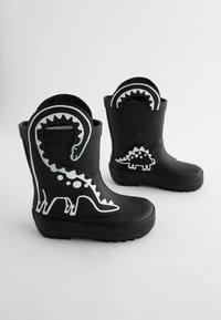 Bottes en caoutchouc noires arborant des motifs de dinosaures blancs, y compris un dinosaure à long cou et un stégosaure, avec des semelles texturées pour une meilleure adhérence.
