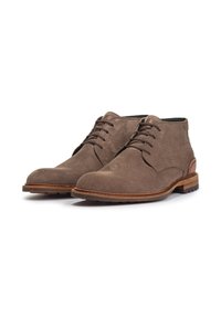 Botas de tobillo de ante marrón con una textura suave, punta redondeada y suela marrón en contraste. Cuenta con cinco ojales y sutiles acentos de costura.