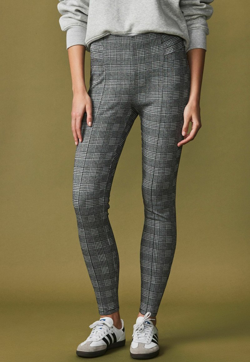 Grå ternede leggings med høj talje og glat tekstur, parret med hvide og grå sneakers med klassiske striber.
