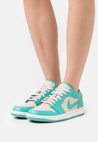 Baskets en cuir turquoise et crème avec semelle blanche, lacets contrastants, logo embossé et texture lisse. Design bas.