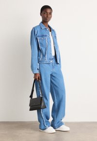 Giubbotto di denim e jeans a gamba larga in azzurro chiaro, con bordi sfilacciati. Abbinati a sneakers bianche e una borsa nera.