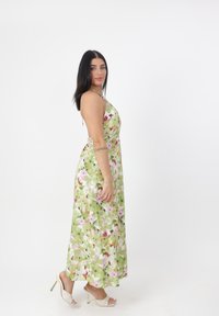Blomster maxikjole med grøn baggrund, prydet med pink og lilla blomster, halterneck og en svajende silhuet. Kombineret med hvide hæle.