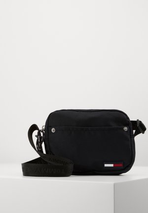 Petit sac bandoulière noir compact avec sangle ajustable et petit logo rectangulaire rouge, blanc et bleu sur la poche avant.