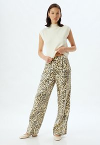 Crème mouwloze top met hoge hals, gecombineerd met wijde broek met een beige en zwarte luipaardprint. Gladde stof en een getailleerde pasvorm.
