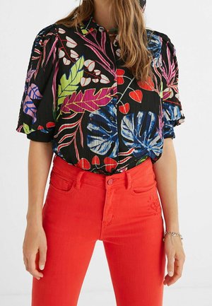 Kwiatowa koszula z krótkim rękawem w kolorze czarnym z kolorowymi wzorami liści; zestawiona z jasnoczerwonymi spodniami o wysokim stanie i srebrną bransoletką.