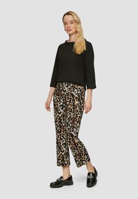 Schwarzes, strukturiertes Oberteil mit 3/4-Ärmeln, kombiniert mit beigen, braunen und schwarzen Leopardendruck-Hosen. Glänzende schwarze Loafers.