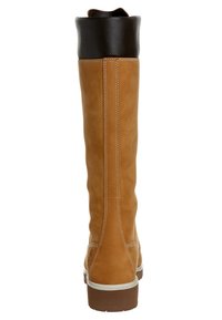 Botas de cuero color tostado hasta la rodilla con un puño de cuero marrón oscuro, costura blanca a lo largo de las costuras y una suela de goma texturizada.