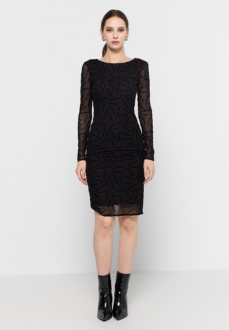 Vestido negro con mangas largas transparentes, que presenta un patrón texturizado de líneas angulares. Silueta ajustada, a la altura de la rodilla, combinado con botas negras brillantes.